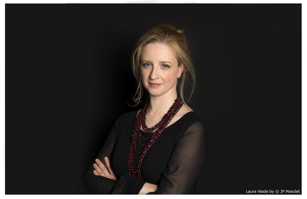 Laura Wade in a black top and a long burgundy beaded necklace, arms folded, against a black background