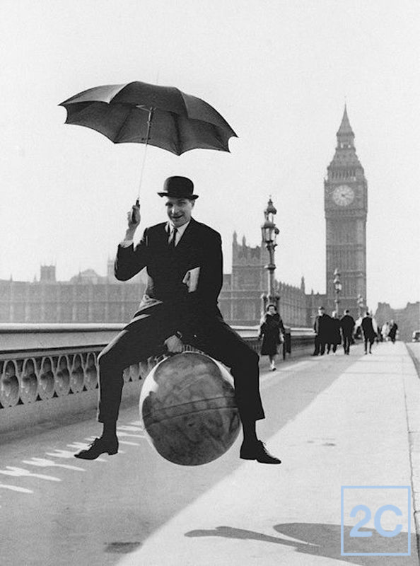 Black and white photo of a man in a bowler hat with an umbrella on a space hopper on Westminster Bridge
