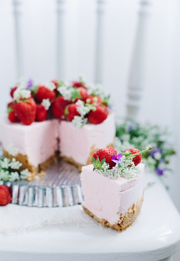 Pink strawberry cheesecake topped with fresh strawberries and white flowers, with one slice cut