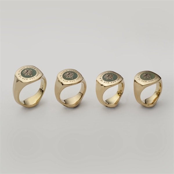 Four yellow gold signet rings with green enamel crest faces, standing in a row