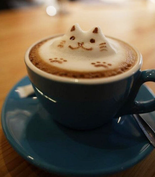 Cappuccino in a blue cup with milk foam shaped like a cat's head and cocoa paw prints