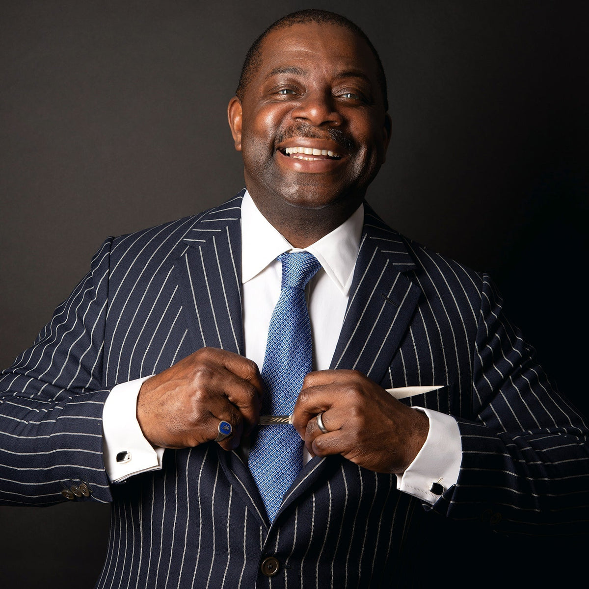 Charlie Allen in a navy pinstripe suit smiling, wearing a ring set with a blue stone and a signet ring