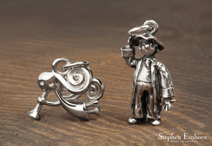 Two silver charms for the Little Angel Theatre: a swirling ram-like figure and a boy in a hat and long coat