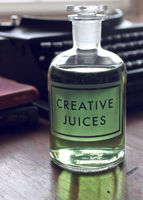 Glass apothecary bottle of green liquid labelled Creative Juices, in front of a vintage typewriter