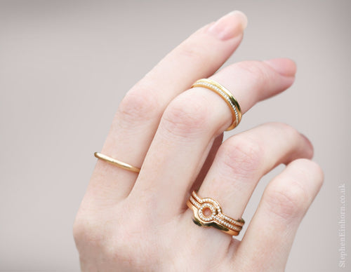 Hand wearing slim gold bands, a micro pave diamond band and a stacked gold ring with a diamond circle