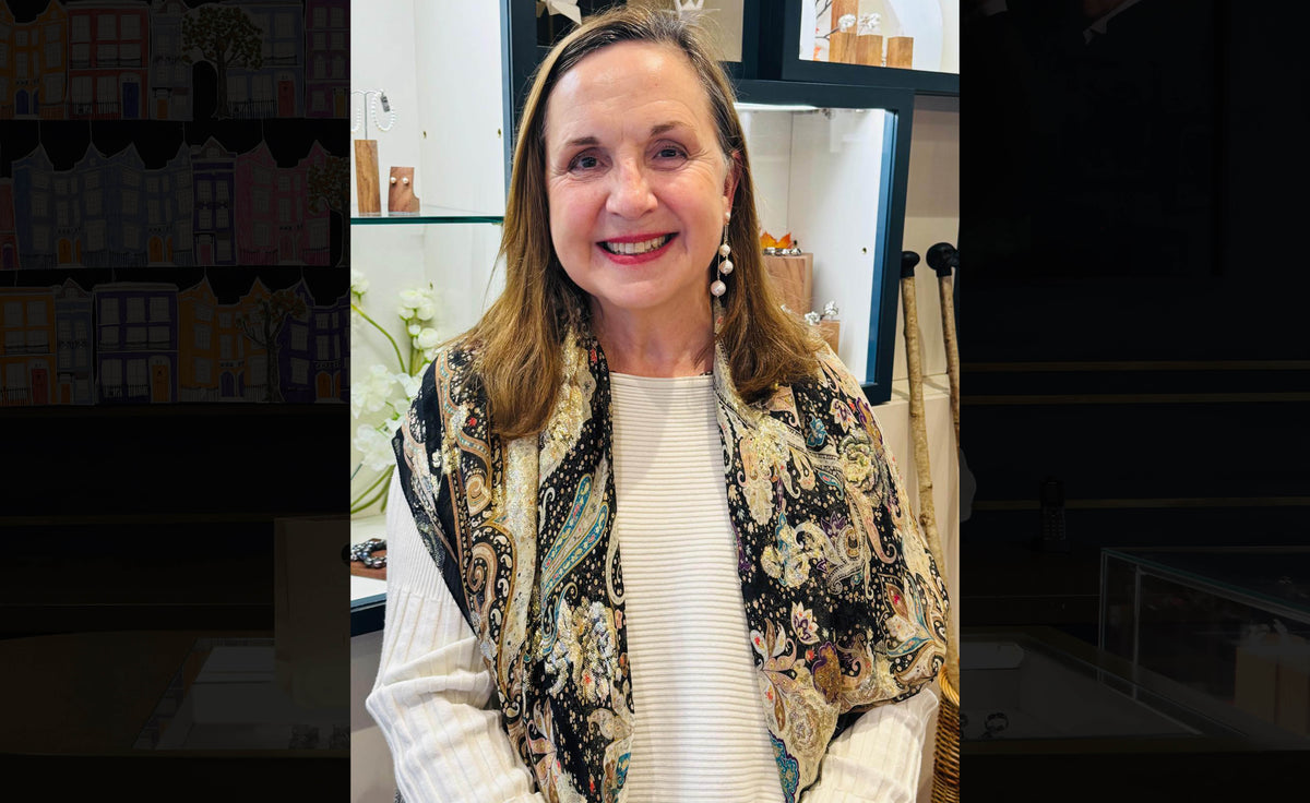 Scientist Debbie Allen smiling in our shop, wearing pearl drop earrings and a paisley scarf