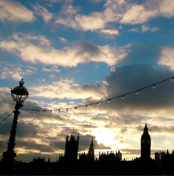 Silhouette of Big Ben and the Houses of Parliament at sunset, with a riverside lamp and string lights