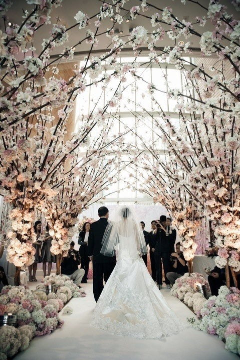 Bride and groom at the end of a white aisle lined with arches of pink and white blossom