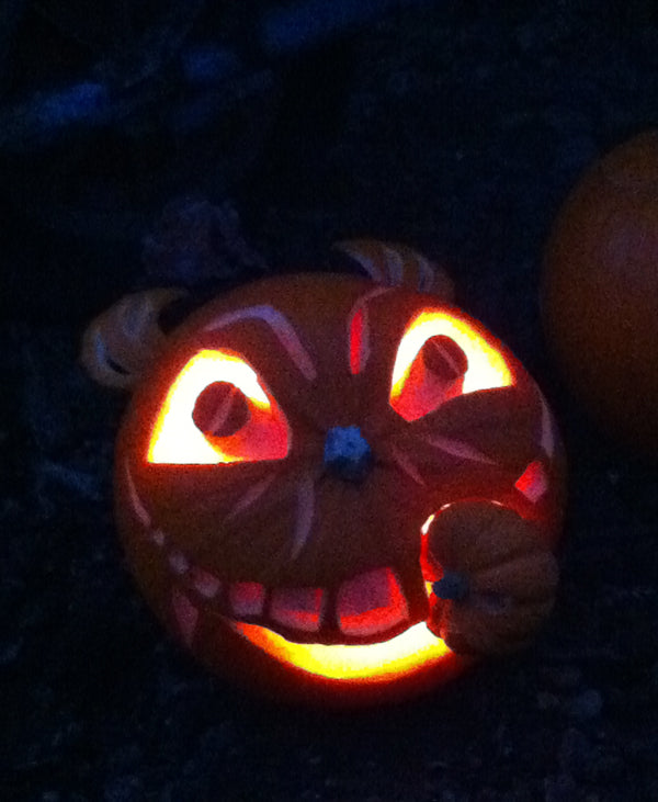 Carved Halloween pumpkin lit from inside, with a grinning face biting a small pumpkin