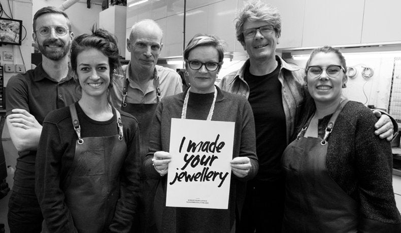 Our workshop team in aprons holding a sign reading I made your jewellery, in black and white
