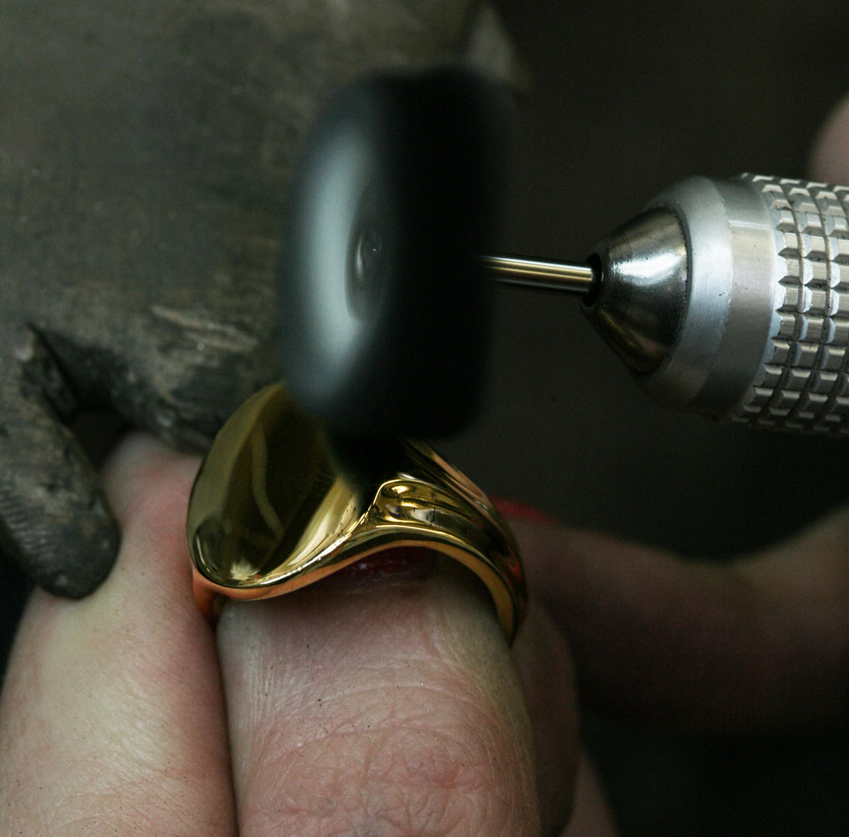 Yellow gold signet ring being polished on a jeweller's finger with a rotary polishing wheel