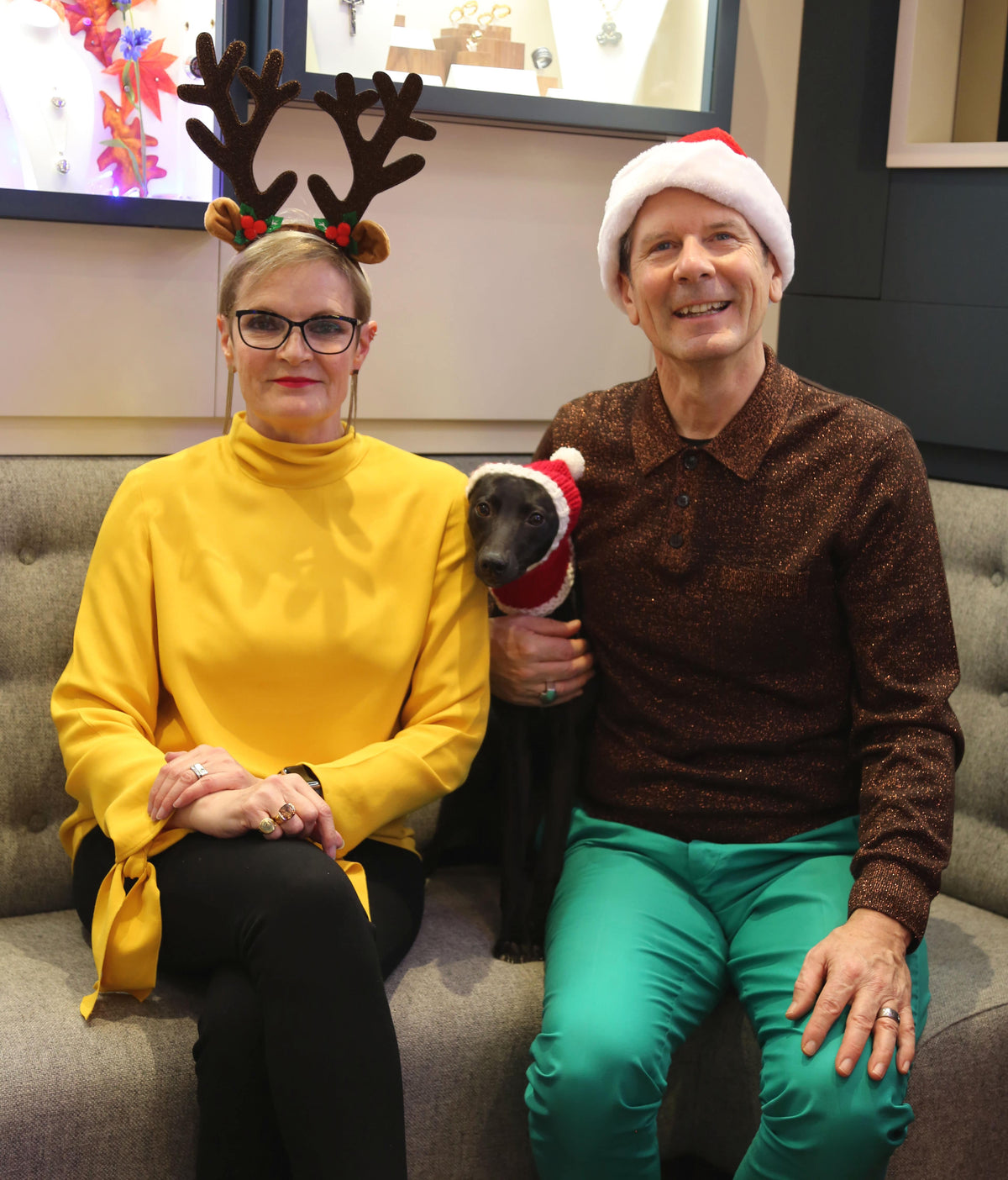 Two people and a dog in festive hats on a grey sofa in our shop, one wearing reindeer antlers