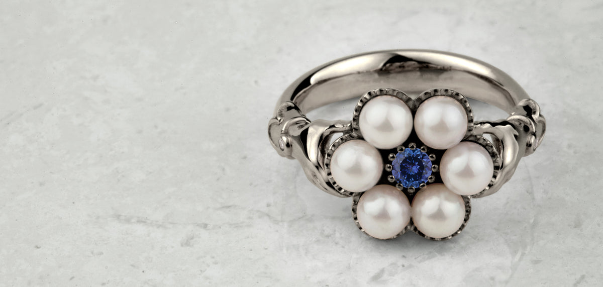 White gold ring with six white pearls set in a flower around a blue sapphire