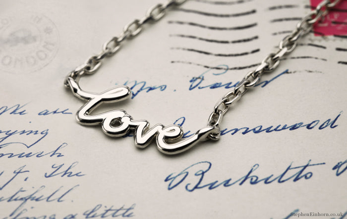Silver 'love' script necklace on a chain, resting on an old handwritten letter