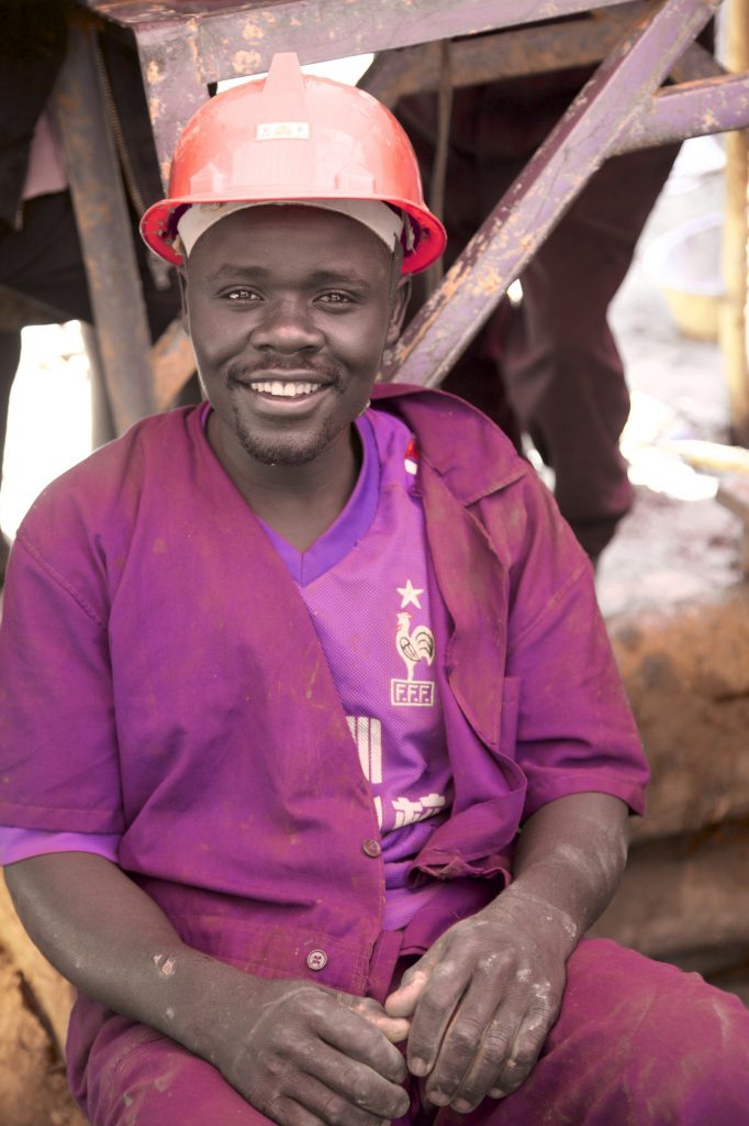 Smiling miner in a red hard hat and purple overalls at a Fairtrade gold mine