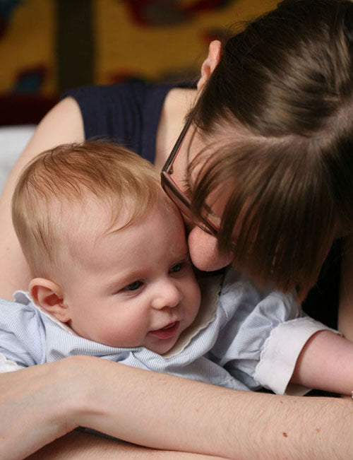 Mother in glasses kissing her smiling baby's head as she holds him close