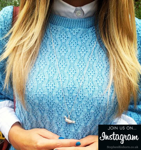 Silver pigeon pendant on a long chain worn over a pale blue cable-knit jumper