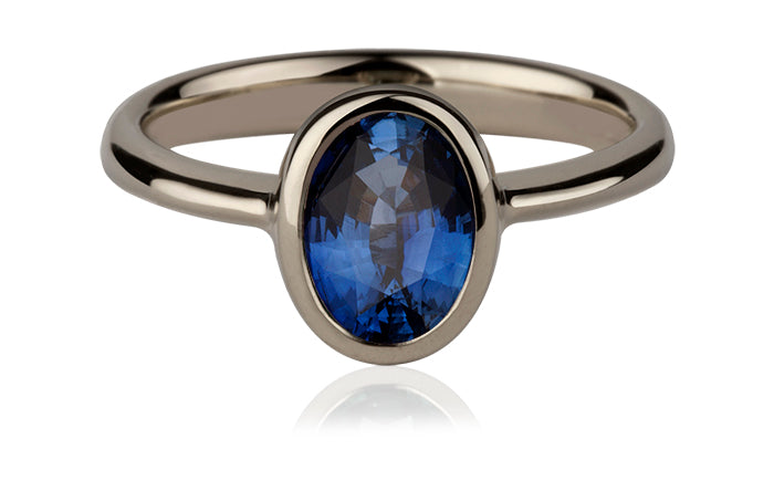 White gold ring set with an oval blue sapphire in a plain bezel
