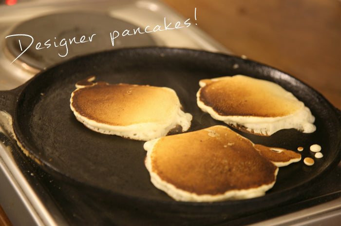 Three pancakes cooking on a black griddle pan, captioned Designer pancakes!