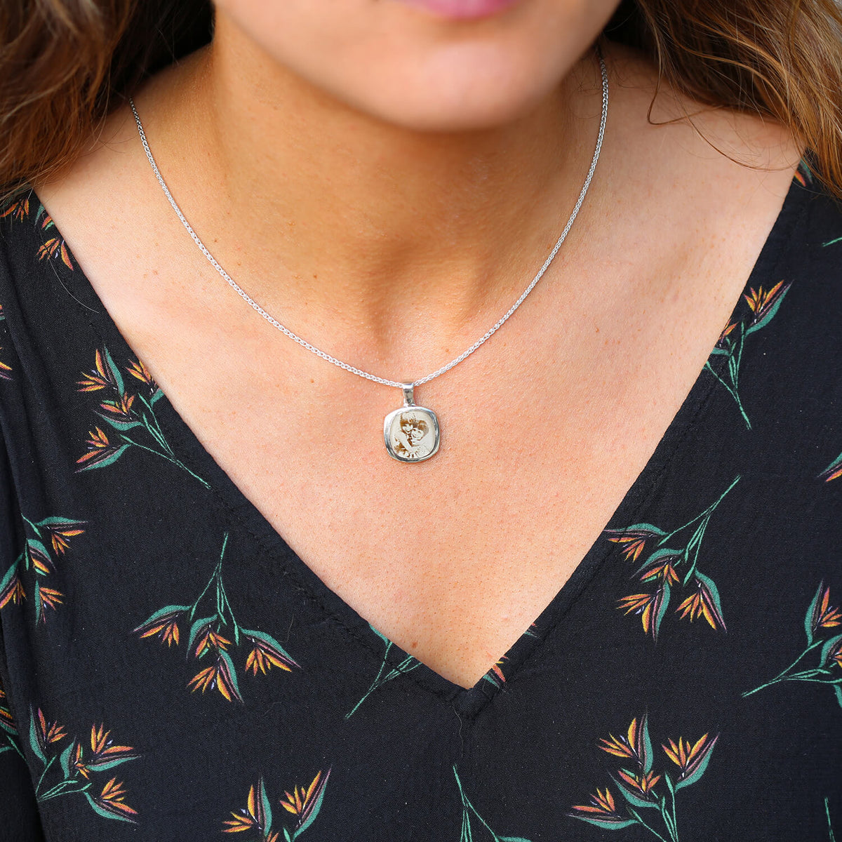Girl in a floral v neck top wearing a silver signet necklace with photo engraving of two children