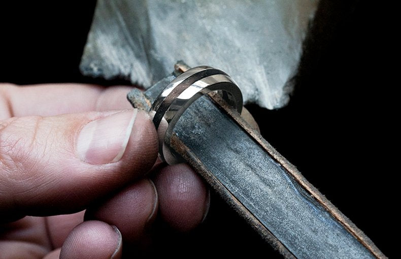 Jeweller's fingers holding a striped two-tone ring on a wooden ring stick in the workshop