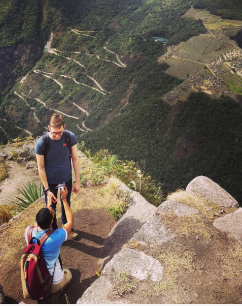 Man kneeling on a mountain path high above Machu Picchu, holding out a ring to his partner