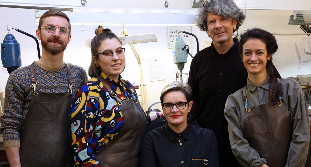 Our team of six standing together in aprons in the Islington workshop, smiling at the camera