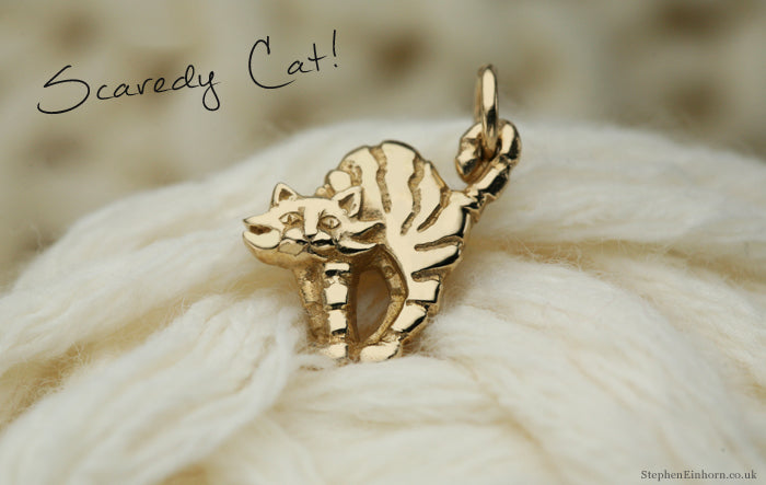 Yellow gold scaredy cat charm with an arched back resting on a ball of cream wool