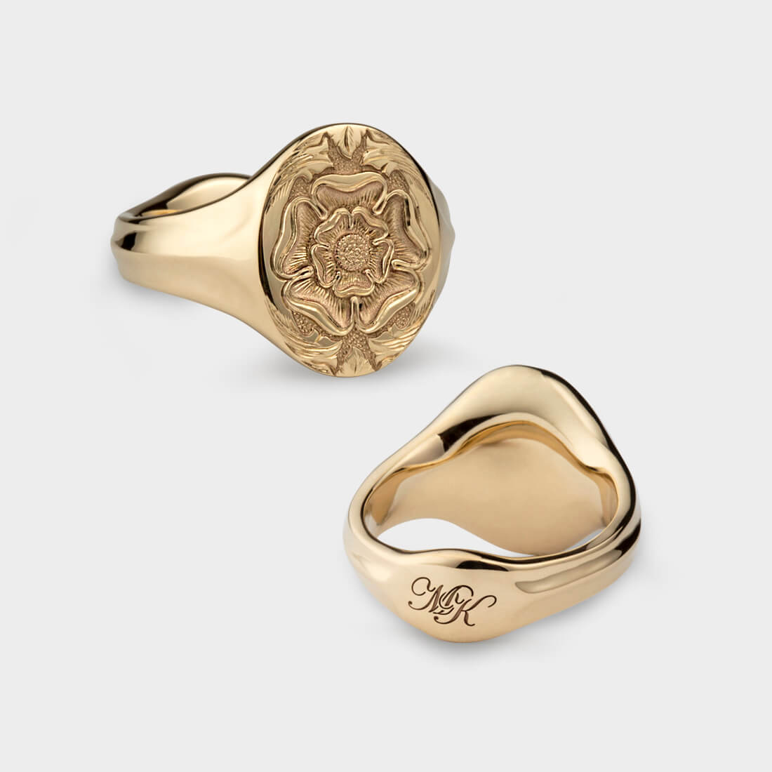 An oval yellow gold signet ring with a seal engraving of a rose and it's back view with an engraving of two initials, MK