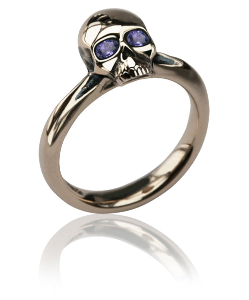 White gold skull ring with tanzanite eyes on a slim plain band, shown on white