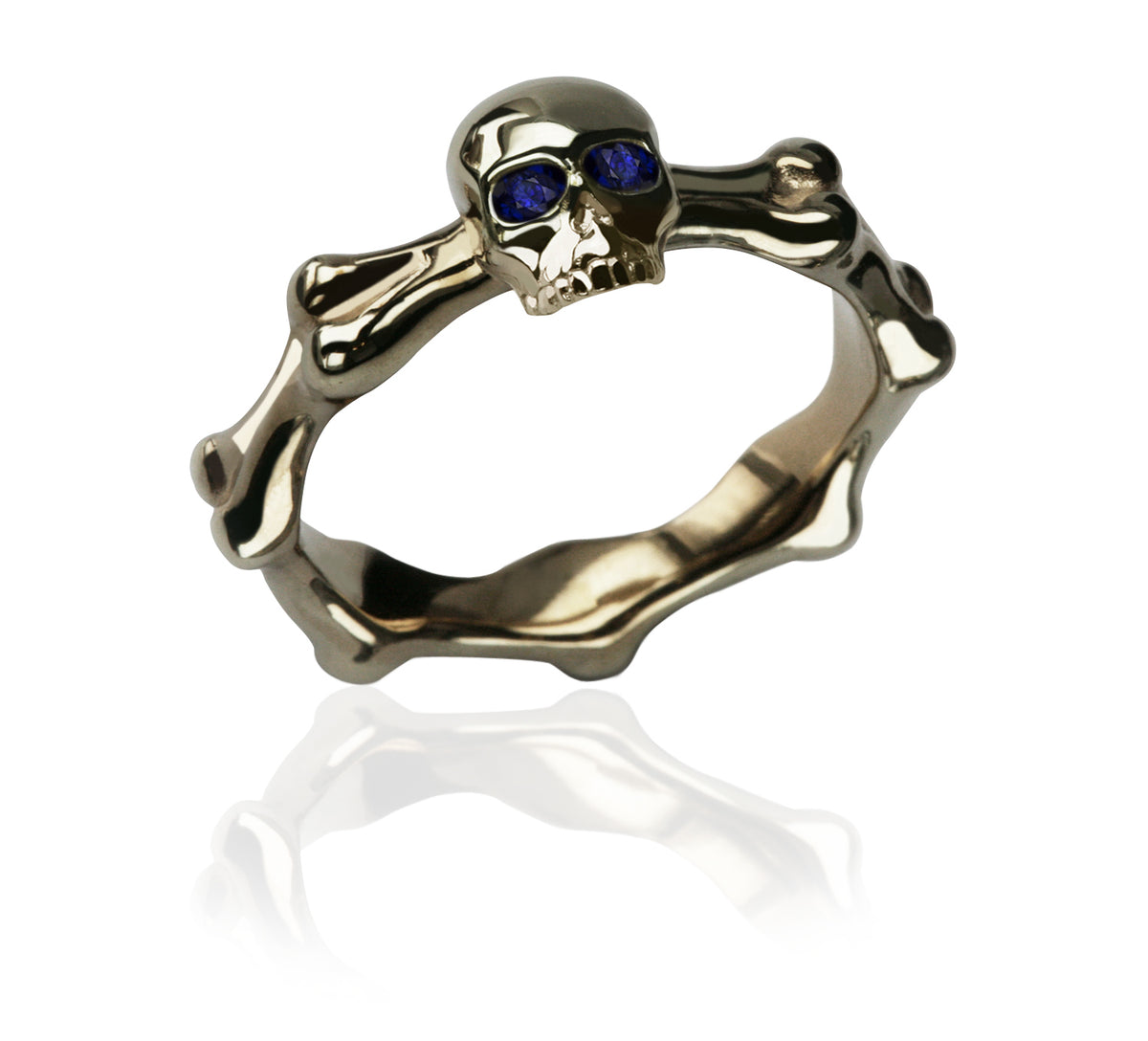 Yellow gold skull and bones ring with blue sapphire eyes, shown on white with its reflection