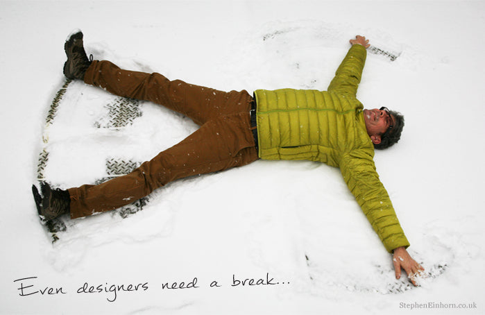Man in a green puffer jacket making a snow angel, captioned 'Even designers need a break'