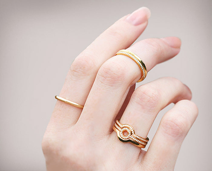 Woman's hand with manicured nails wearing a stack of slim gold rings, some set with diamonds