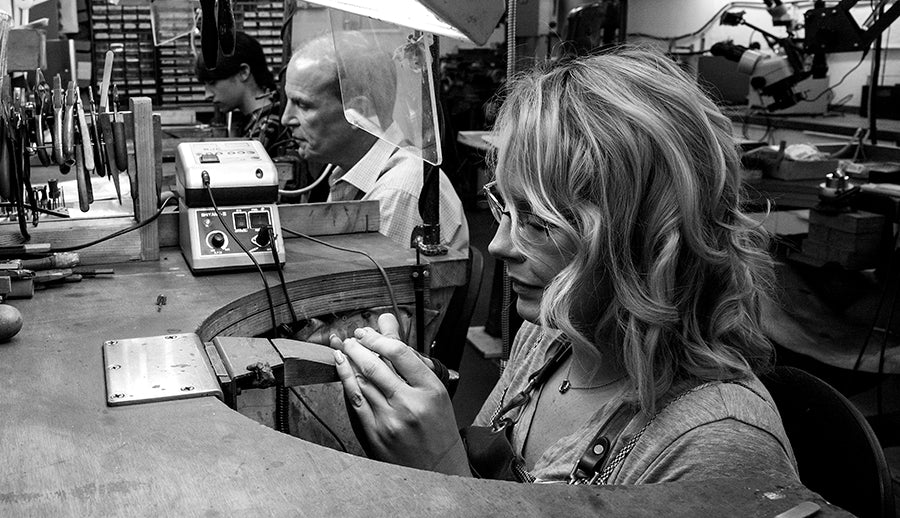 Jewellers at their benches in our London workshop, a woman working on a piece in the foreground, black and white