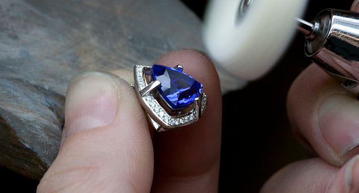Trilliant cut tanzanite ring with a diamond set white gold surround being polished in the workshop