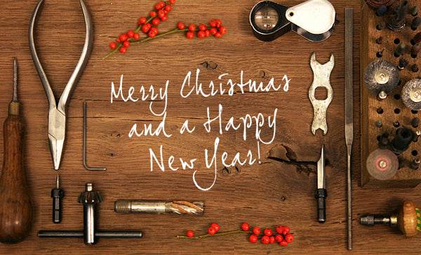 'Merry Christmas and a Happy New Year' written on a wooden bench laid with jeweller's tools and red berries