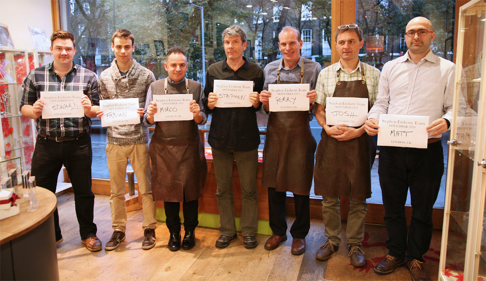 Seven members of Team Einhorn, several in leather aprons, holding Movember name signs in the shop