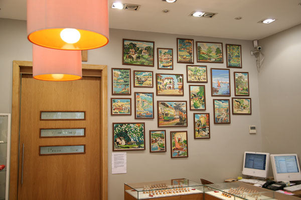 Framed paintings hung on the wall of the Stephen Einhorn showroom above glass jewellery cabinets, lit by orange lamps
