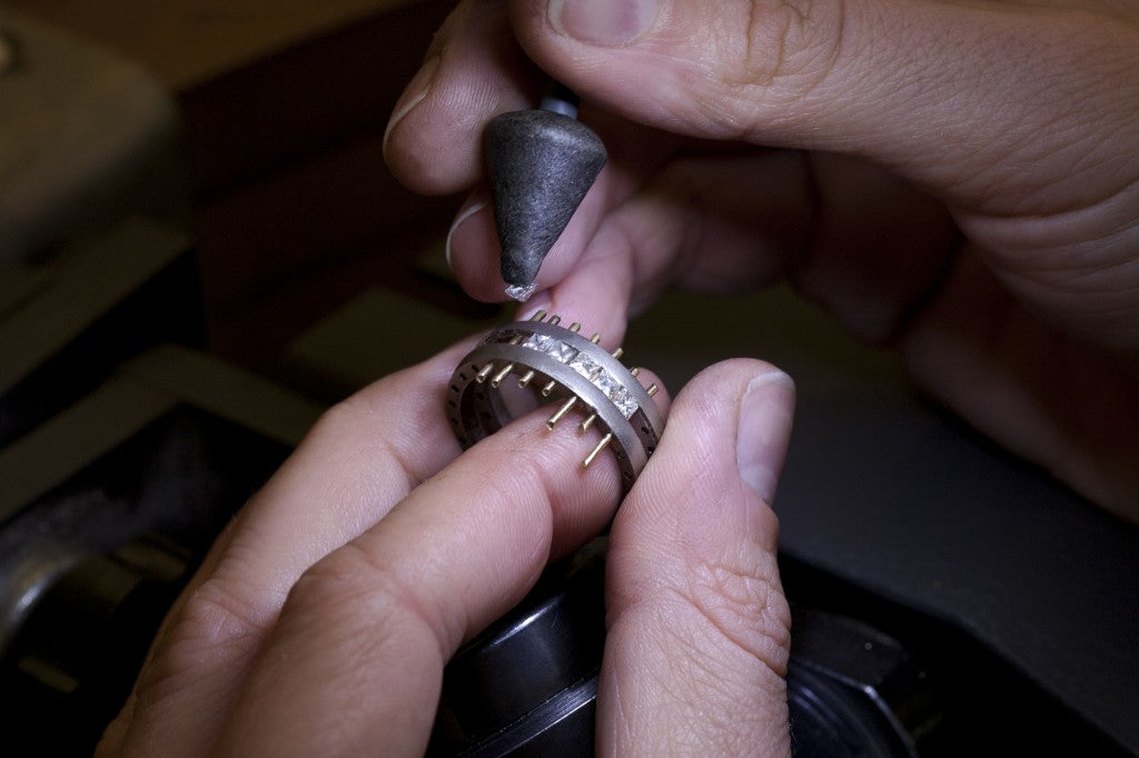 Jeweller holding a gold ring with pins in place for stone setting, next to a polishing tool