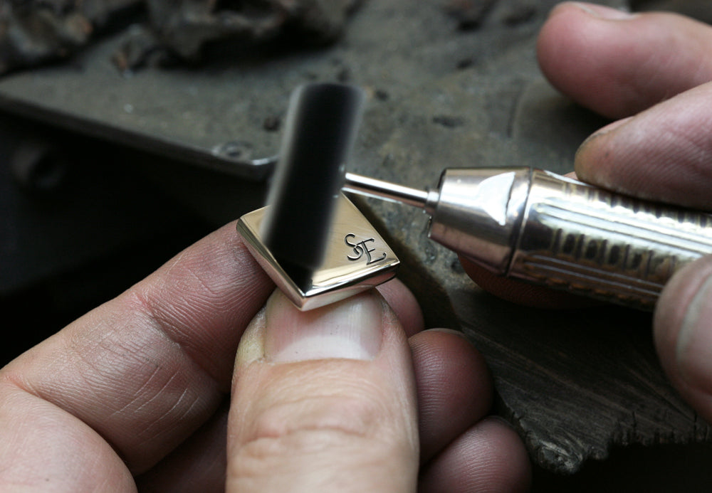 Silver cufflink engraved with SE initials being polished by hand with a rotary polishing wheel