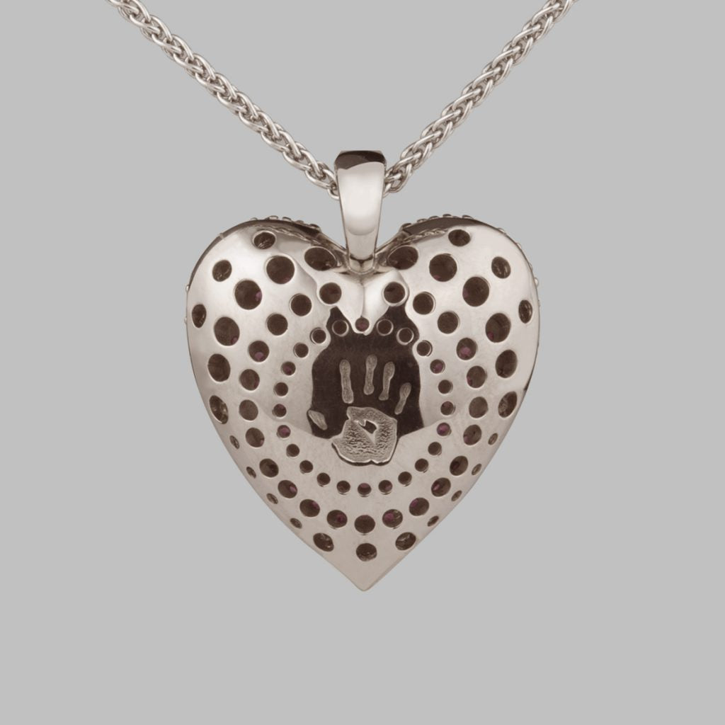 Back of a silver heart pendant with pierced dots and a stamped handprint, on a silver chain