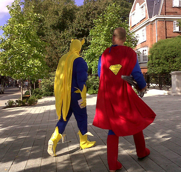 Two men dressed as Superman and Bananaman walking along a sunny Islington street