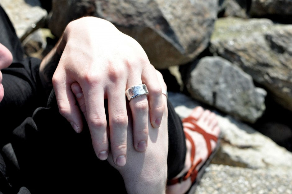 Hand wearing a wide beaten sterling silver ring, resting on a knee against rocks in the sun