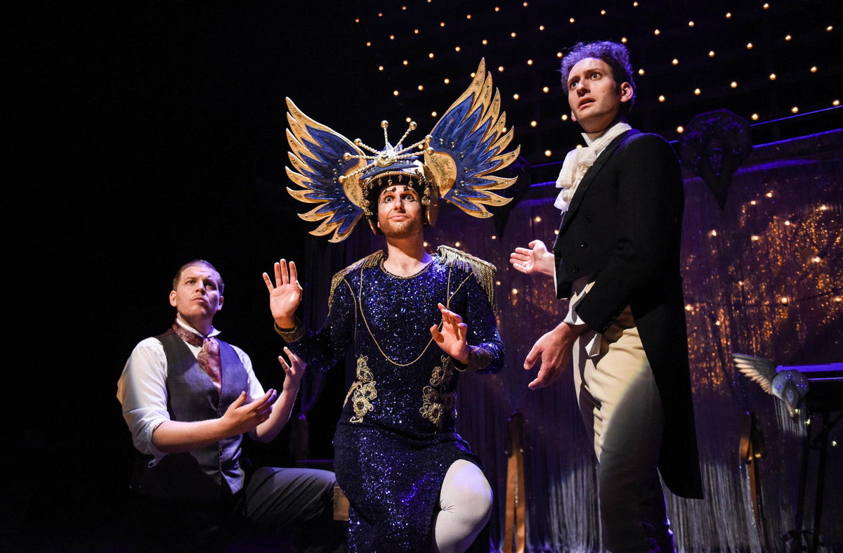 Actors on stage in How to Win Against History, one in a sequinned gown and a winged golden headdress