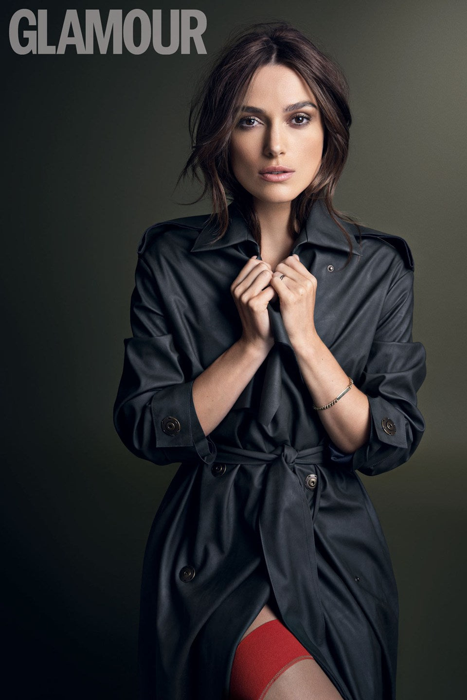 Keira Knightley in a dark trench coat on a Glamour magazine shoot, wearing a fine gold ID bracelet