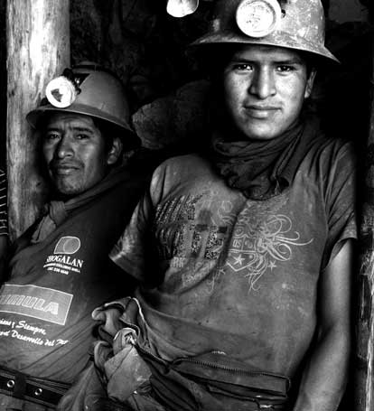 Two miners in hard hats with headlamps underground, in black and white