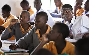 Secondary school students in yellow and grey uniforms listening in a classroom