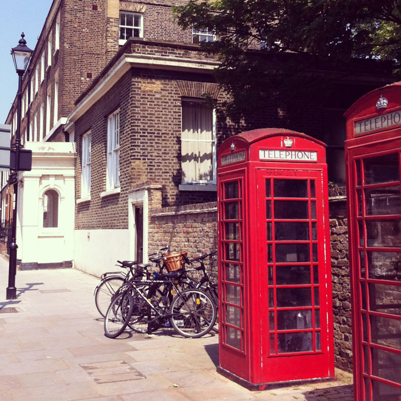 Two red telephone boxes on a sunny London street beside a brick Georgian house and parked bicycles