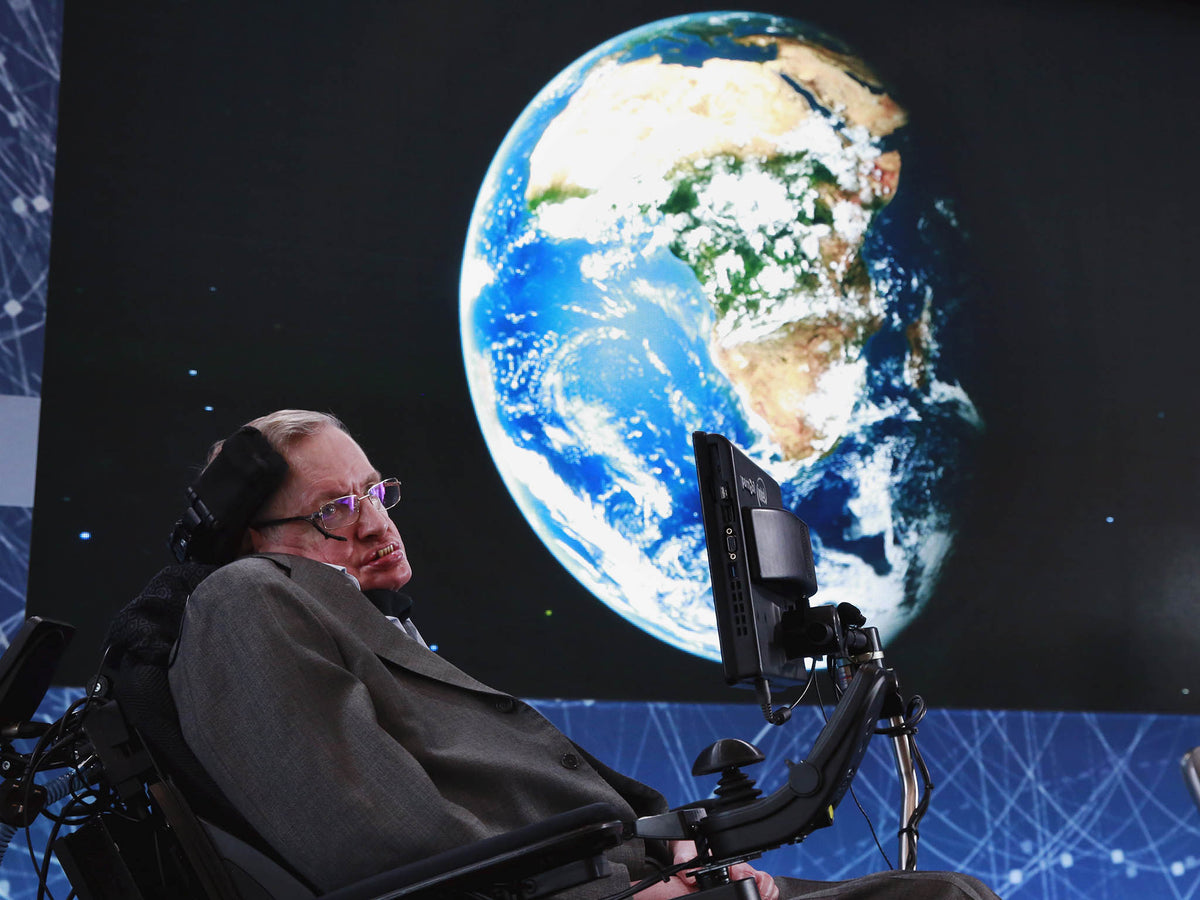 Stephen Hawking in his wheelchair on stage in front of a large projected image of the Earth