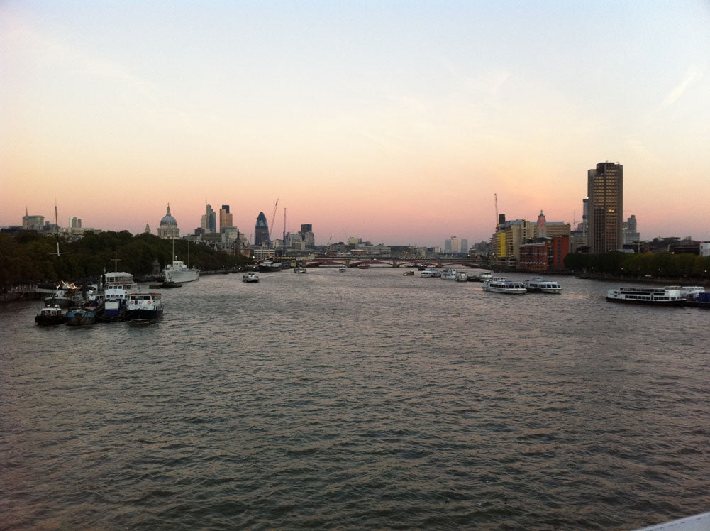 The Thames at sunset from a bridge, boats moored and the City skyline with St Paul's in the distance